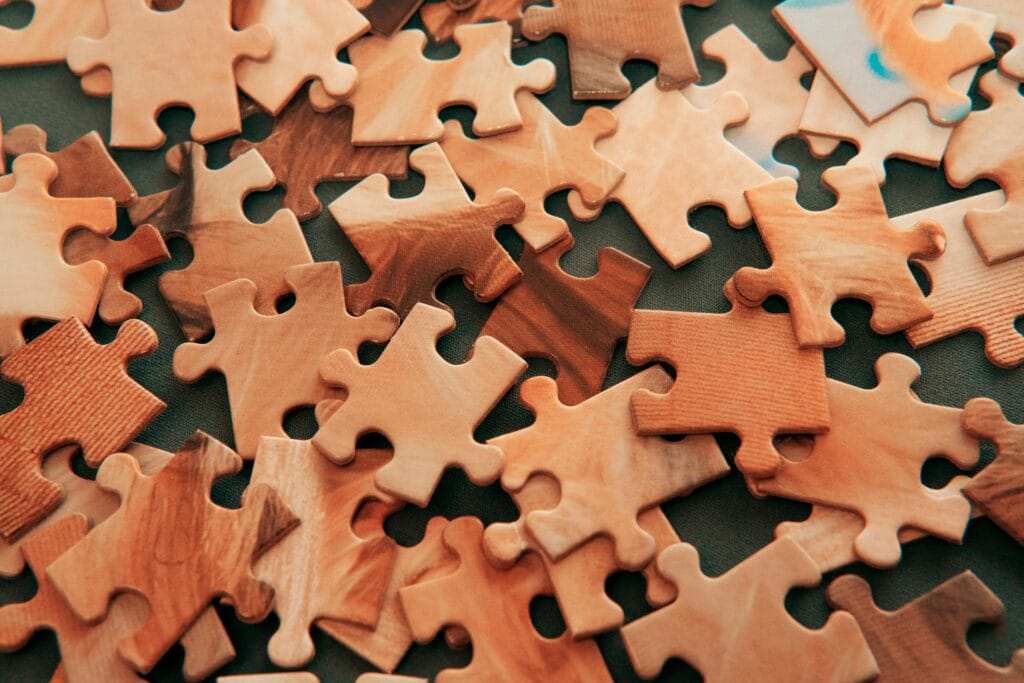 pexels-photo-3852577-3852577 A close-up view of scattered wooden jigsaw puzzle pieces on a dark surface.